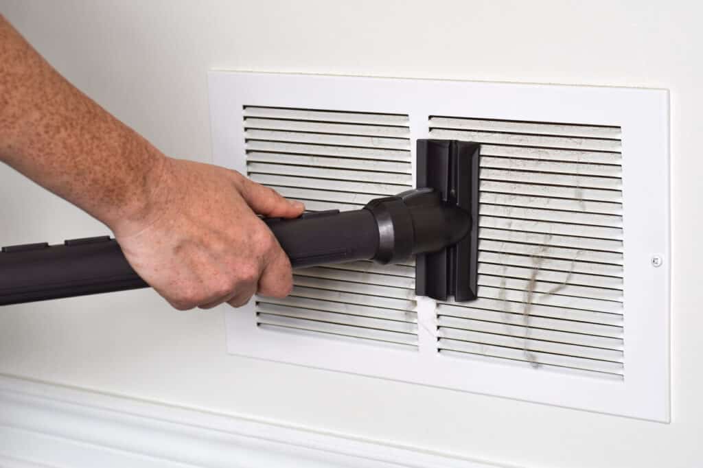 Technician vacuuming a dirty return air vent during duct cleaning