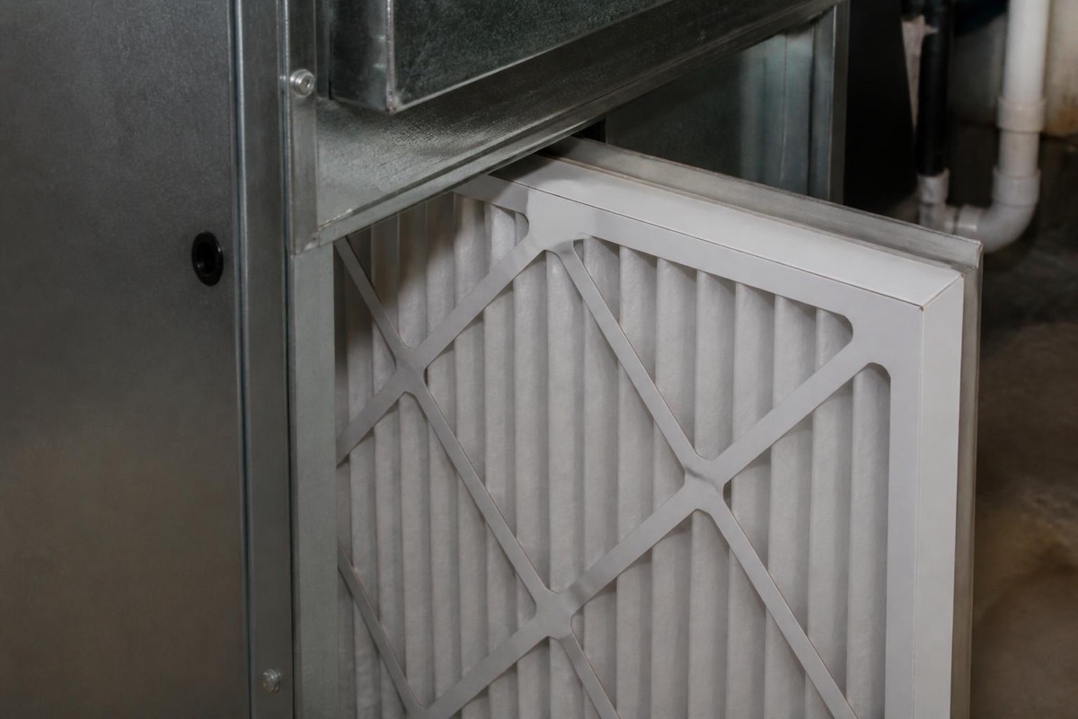 Close up of a clean pleated furnace air filter partially inserted into a metal duct housing.