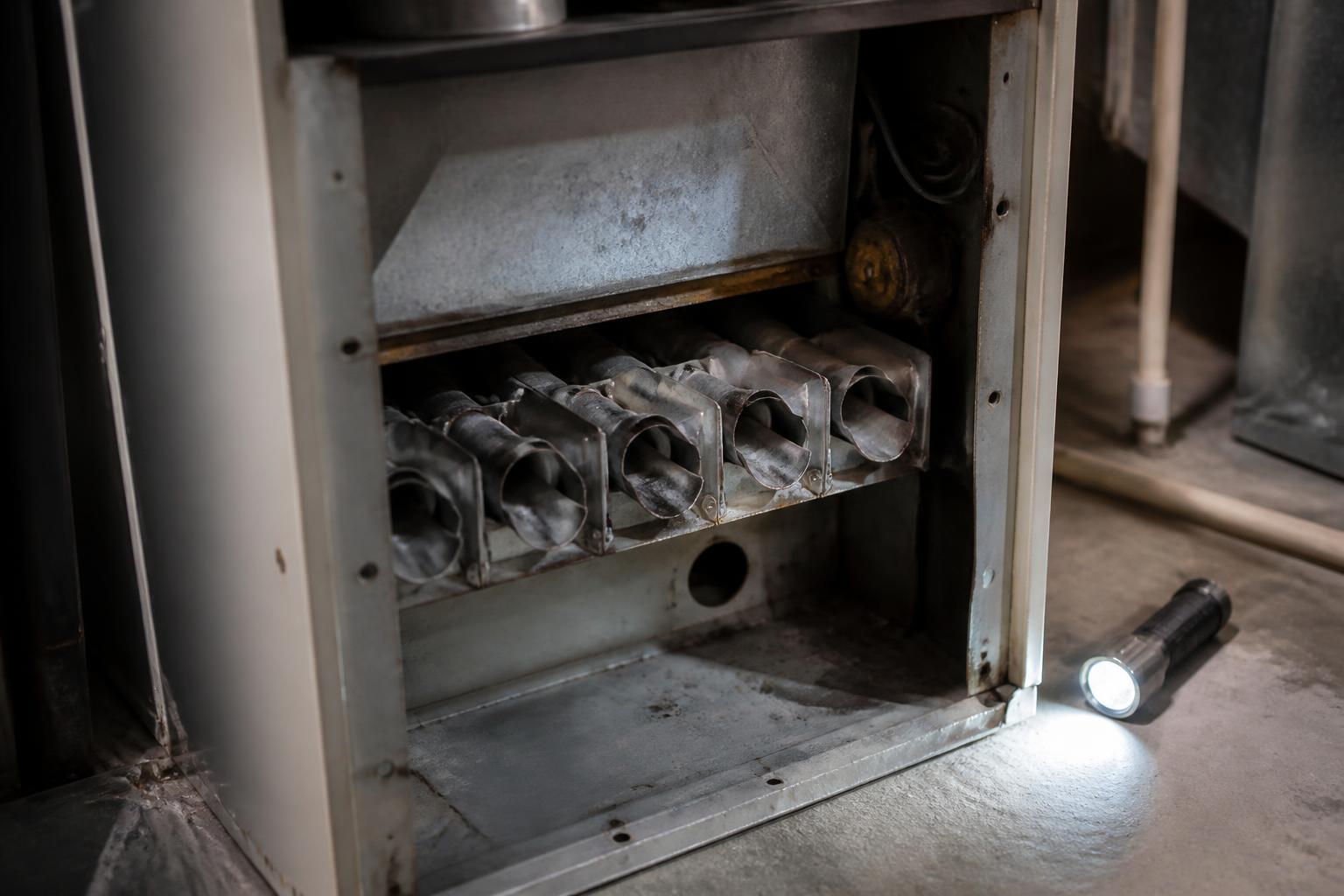 Open furnace burner compartment showing the metal heat exchanger cells with a flashlight nearby