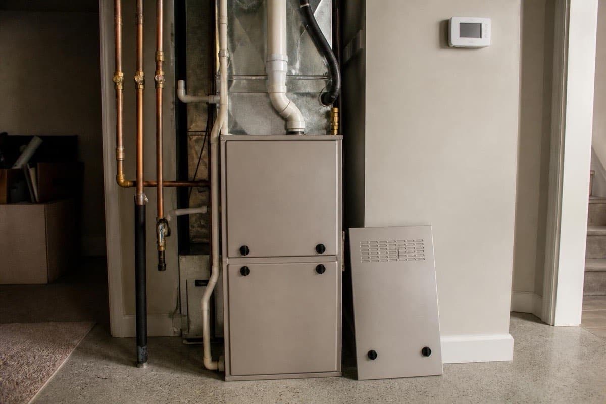 Residential gas furnace cabinet with an open service panel door in a basement mechanical room