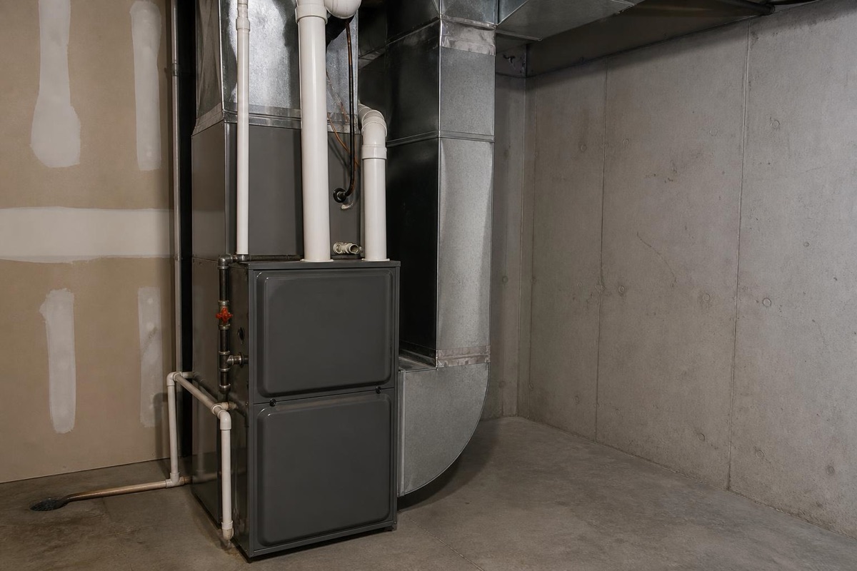 Gas furnace unit connected to sheet metal ductwork in a home mechanical utility room with a concrete floor.