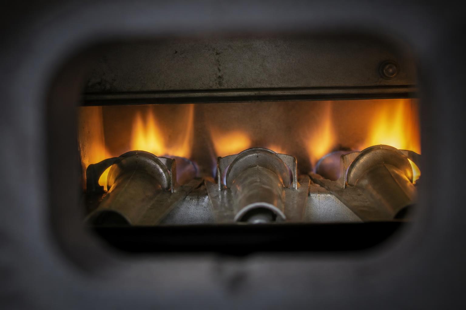 Close-up of uneven yellow-orange gas burner flames visible through a furnace observation opening