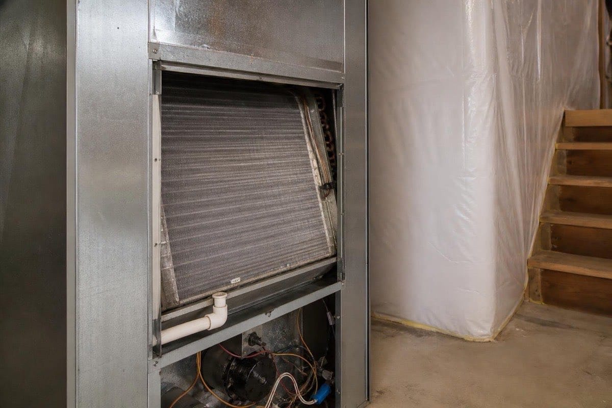 Residential air conditioner evaporator coil compartment with access panel removed, showing a clean coil and drain line