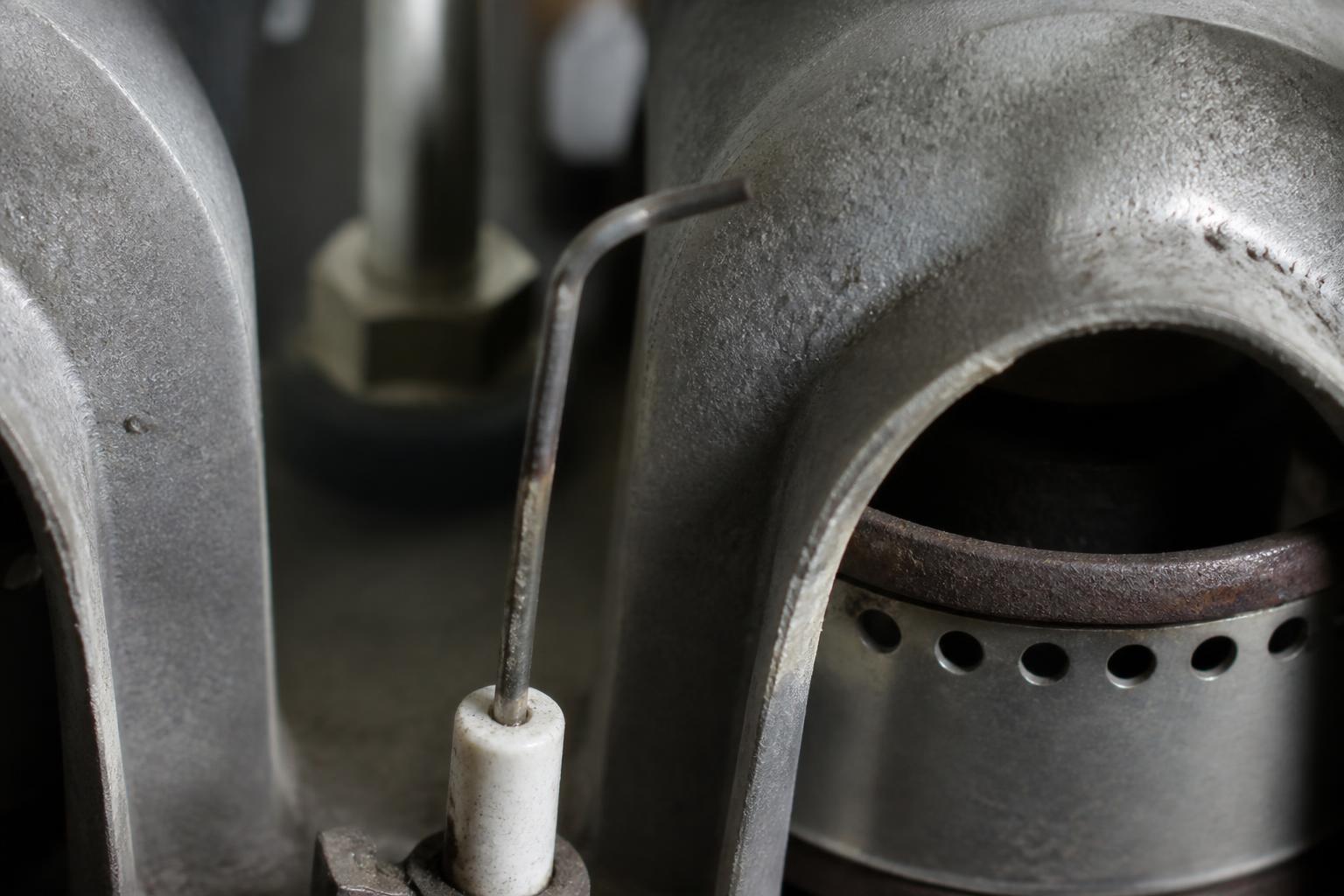 Close-up of a furnace flame sensor rod positioned beside the burner ports