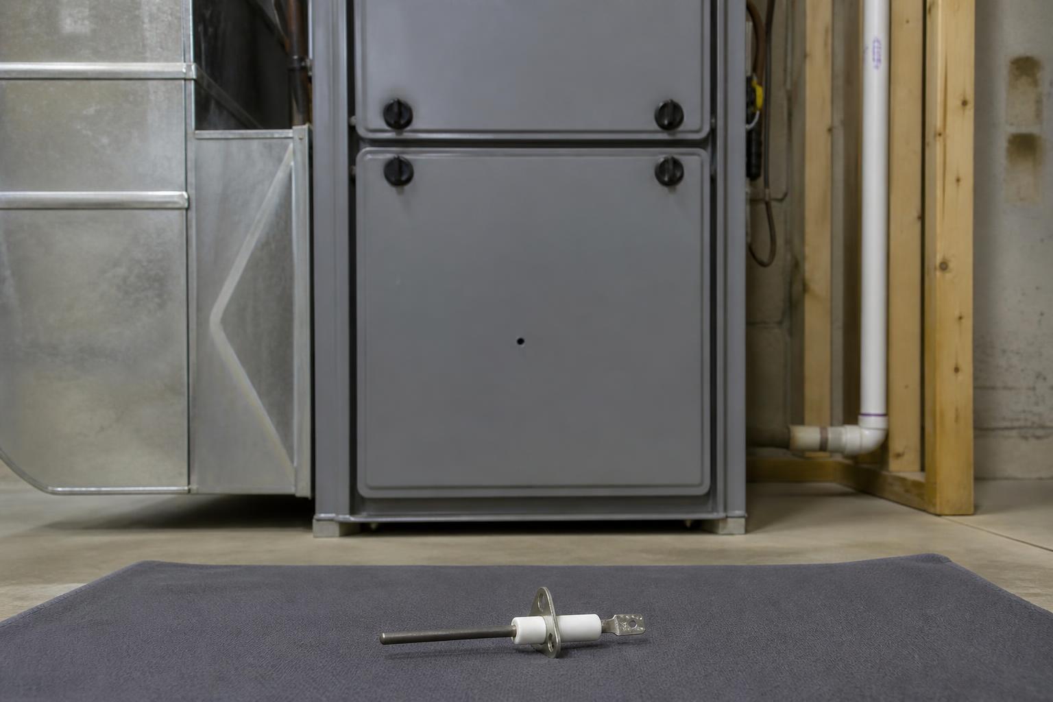 Physically accurate replacement furnace flame-sensor assembly resting in front of a closed residential furnace