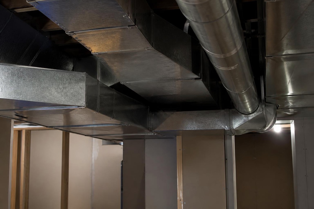 Sheet metal HVAC ductwork and round duct pipe running along the ceiling of an unfinished home basement
