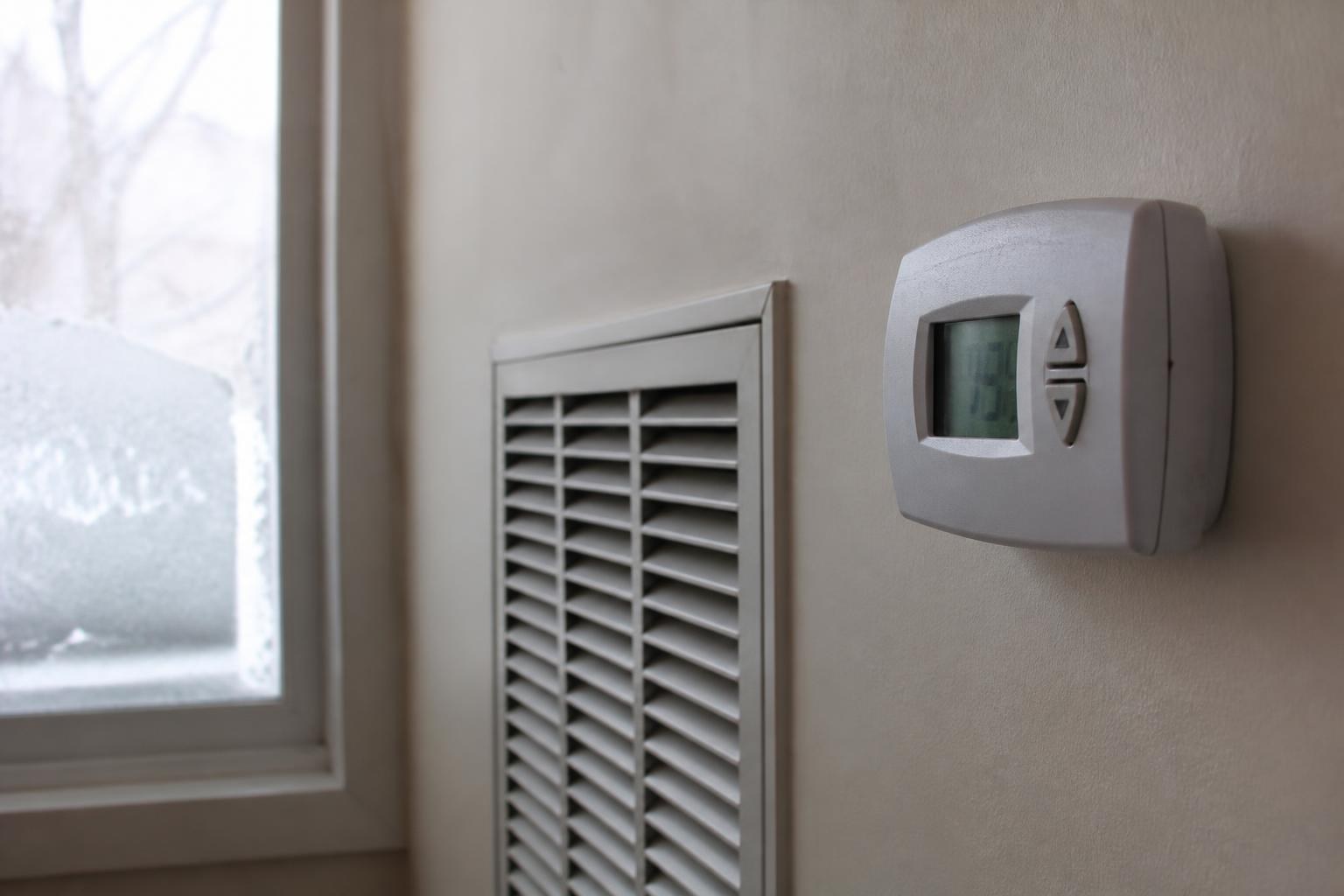Wall thermostat and vent grille beside a frost-covered window in winter